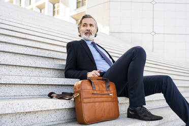 Geschäftsmann mit Bart sitzt mit Tasche auf Stufen - OIPF01964