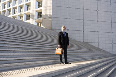 Mature businessman holding bag standing on steps - OIPF01971