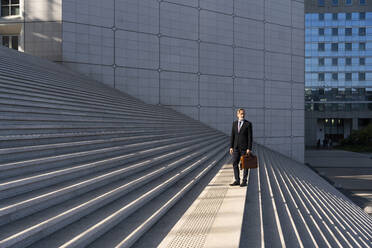 Geschäftsmann mit Tasche auf einer Treppe vor einem Gebäude stehend - OIPF01979