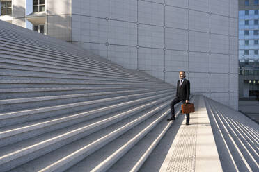 Älterer Geschäftsmann mit Tasche auf einer Treppe stehend - OIPF01981