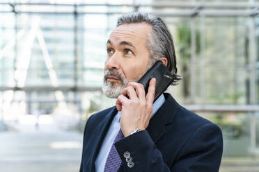 Lächelnder Geschäftsmann mit grauem Haar, der mit einem Smartphone telefoniert - OIPF01991