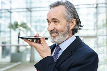 Happy businessman with gray hair sending voicemail through smart phone - OIPF01992