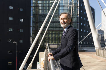 Smiling mature businessman standing by railing on sunny day - OIPF01997