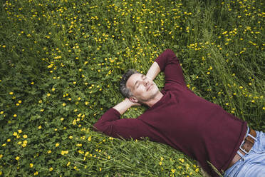 Mature man lying amidst yellow wildflowers on grass at park - UUF26252