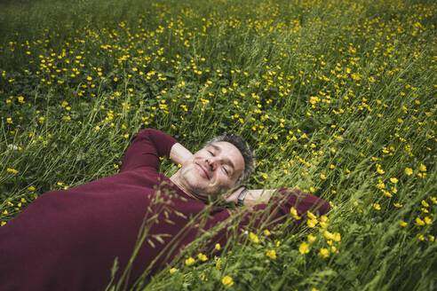 Lächelnder reifer Mann mit Händen hinter dem Kopf im Gras liegend - UUF26253