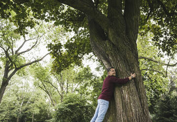Glücklicher Mann, der einen Baum im Park umarmt - UUF26256