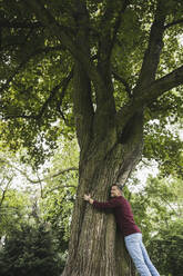 Glücklicher reifer Mann, der einen Baum im Park umarmt - UUF26257