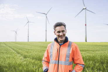 Smiling engineer in reflective clothing standing on field - UUF26278