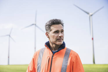 Engineer wearing reflective clothing in front of wind turbines on field - UUF26280