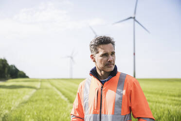 Engineer standing in front of wind turbine on sunny day - UUF26281