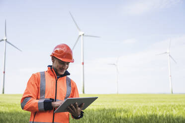 Lächelnder Ingenieur mit Tablet-PC auf einem Feld stehend - UUF26294