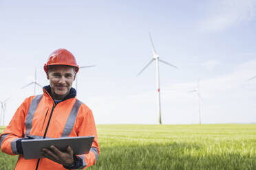 Lächelnder reifer Ingenieur mit Tablet-PC auf einem Feld stehend - UUF26295