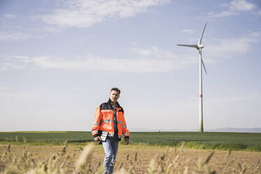 Engineer wearing reflective clothing holding tablet PC walking on field - UUF26307