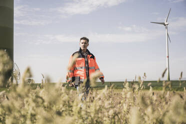 Mature engineer wearing reflective clothing walking in field on sunny day - UUF26311