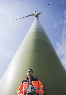 Ingenieur vor einer großen Windkraftanlage an einem sonnigen Tag - UUF26313