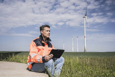 Ingenieur mit Tablet-PC in der Nähe einer Windkraftanlage auf einem Feld - UUF26315