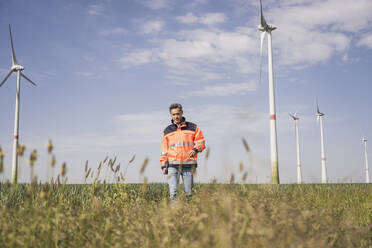 Engineer walking amidst crops in field on sunny day - UUF26316