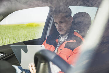 Ingenieur mit Laptop im Auto sitzend durch die Windschutzscheibe gesehen - UUF26321