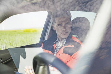 Ingenieur mit Laptop im Auto sitzend durch die Windschutzscheibe gesehen - UUF26322