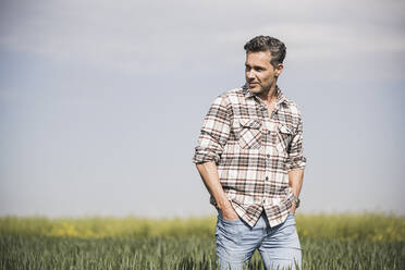 Mature man with hands in pockets walking at field on sunny day - UUF26329