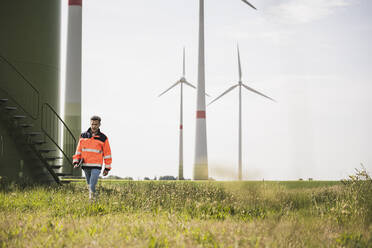 Engineer walking in front of wind turbines on field - UUF26336