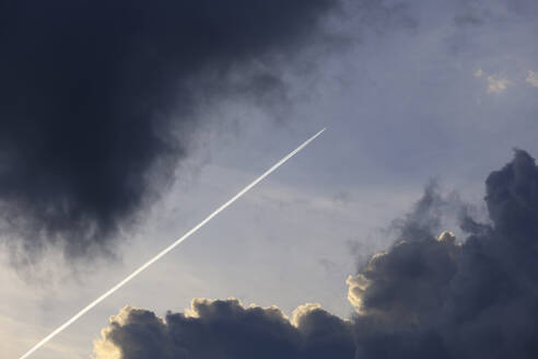 Flugzeug hinterlässt Kondensstreifen zwischen dunklen Wolken - JTF02077