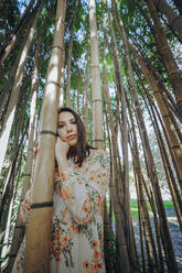 Contemplative young woman standing in bamboo grove - OMIF00843