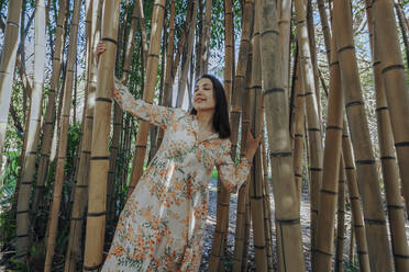 Woman with eyes closed standing in bamboo grove - OMIF00845