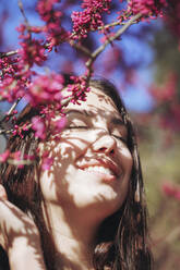 Glückliche junge Frau mit geschlossenen Augen bei rosa Blumen - OMIF00847