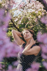 Schöne Frau mit geschlossenen Augen im Garten stehend an einem sonnigen Tag - OMIF00854