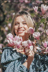 Lächelnde Frau neben rosa Blumen an einem sonnigen Tag - OMIF00858