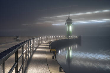 Germany, Schleswig-Holstein, Lubeck, Long exposure of ferry passing Travemunde lighthouse at foggy night - KEBF02300
