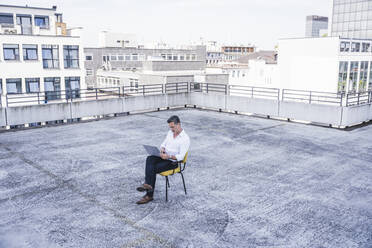 Geschäftsmann mit Laptop auf der Terrasse eines Gebäudes sitzend - UUF26346
