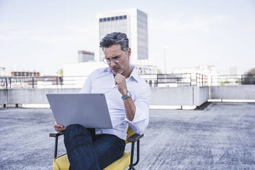 Geschäftsmann mit Brille und Laptop auf der Terrasse eines Gebäudes sitzend - UUF26348