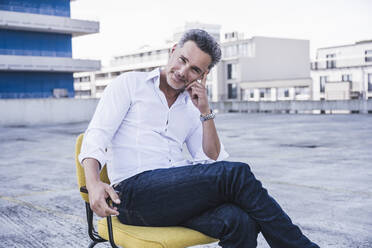 Lächelnder Geschäftsmann auf der Terrasse eines Gebäudes sitzend - UUF26356