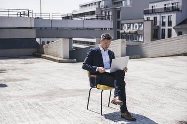 Geschäftsmann mit Laptop auf der Terrasse eines Gebäudes sitzend - UUF26364
