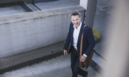 Smiling mature businessman with bag walking at parking garage - UUF26370