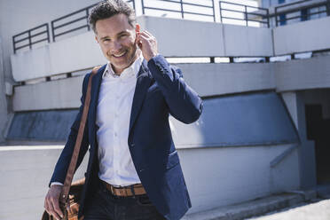 Happy businessman with bag walking at parking garage on sunny day - UUF26372