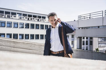 Glücklicher Geschäftsmann mit In-Ear-Kopfhörern im Parkhaus an einem sonnigen Tag - UUF26373