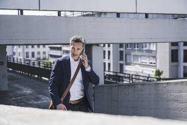 Geschäftsmann, der in einem Parkhaus mit seinem Smartphone telefoniert - UUF26378