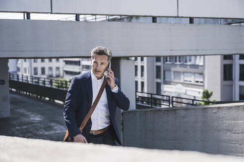 Businessman talking on smart phone walking at parking garage - UUF26378