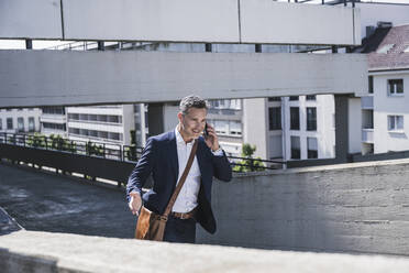 Smiling mature businessman talking on mobile phone at parking garage - UUF26379