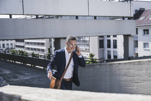 Smiling mature businessman talking on mobile phone at parking garage - UUF26379