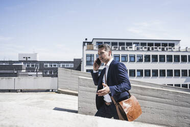 Älterer Geschäftsmann, der mit seinem Handy spricht, während er in einem Parkhaus an einem sonnigen Tag spazieren geht - UUF26380