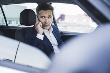 Businessman talking on smart phone sitting in car - UUF26384