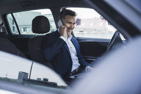 Glücklicher Geschäftsmann, der auf dem Fahrersitz im Auto sitzt und mit seinem Smartphone spricht - UUF26385