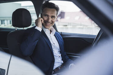Smiling mature businessman talking on mobile phone sitting in car - UUF26386