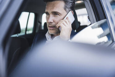 Älterer Geschäftsmann, der im Auto sitzend mit seinem Smartphone telefoniert - UUF26387