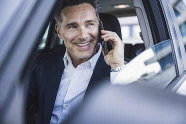 Glücklicher Geschäftsmann, der im Auto mit seinem Handy telefoniert - UUF26388