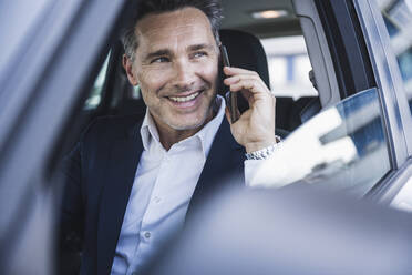 Happy businessman talking on mobile phone in car - UUF26388